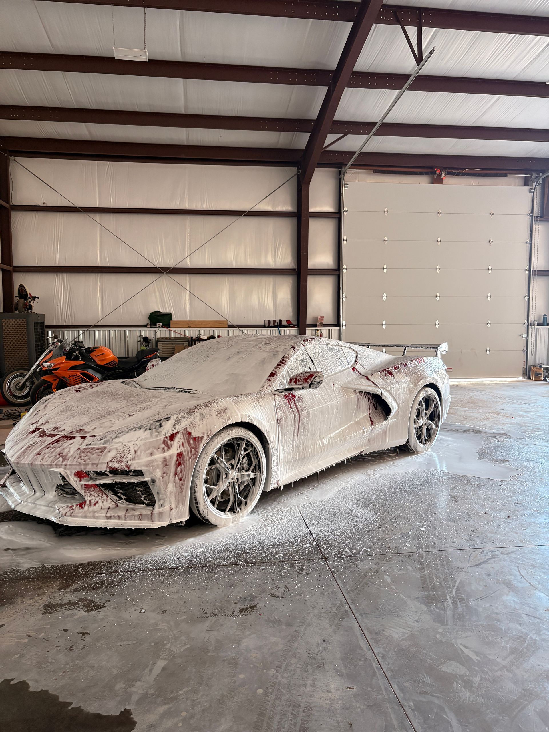 Sports car covered in foam inside a metal garage with a large white door