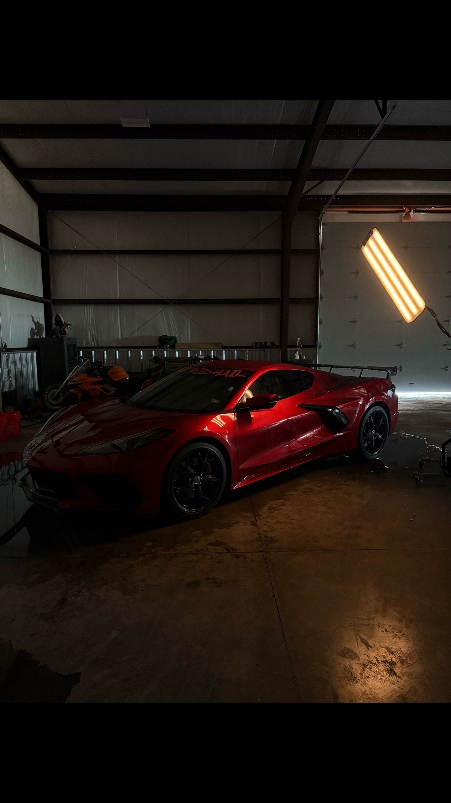 Red sports car parked in a dim garage with bright wall lights reflecting on the wet floor.