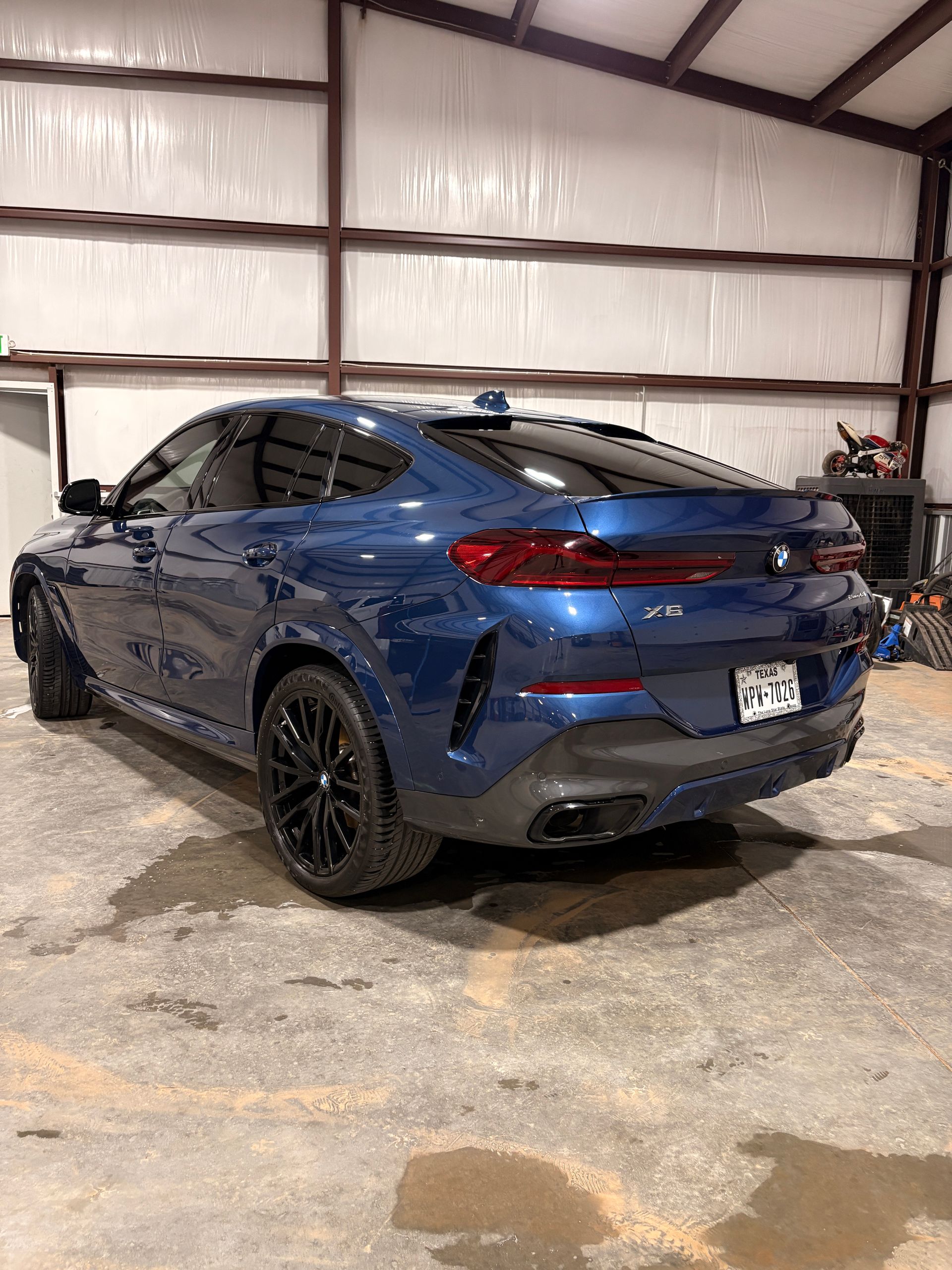 Blue sports sedan parked inside a warehouse garage, rear three-quarter view
