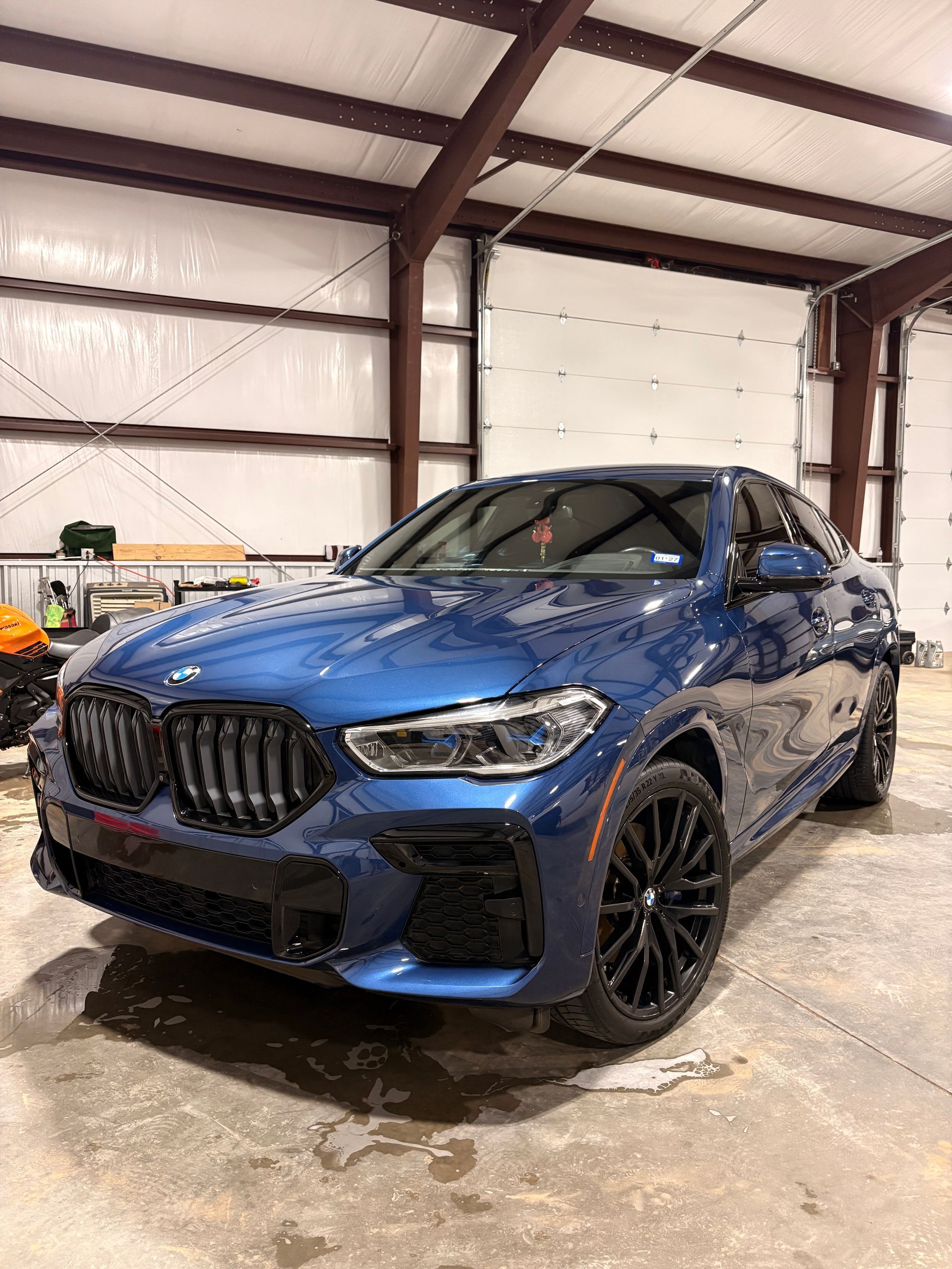 Blue BMW SUV in a garage, shown from the front-left angle on a wet concrete floor.