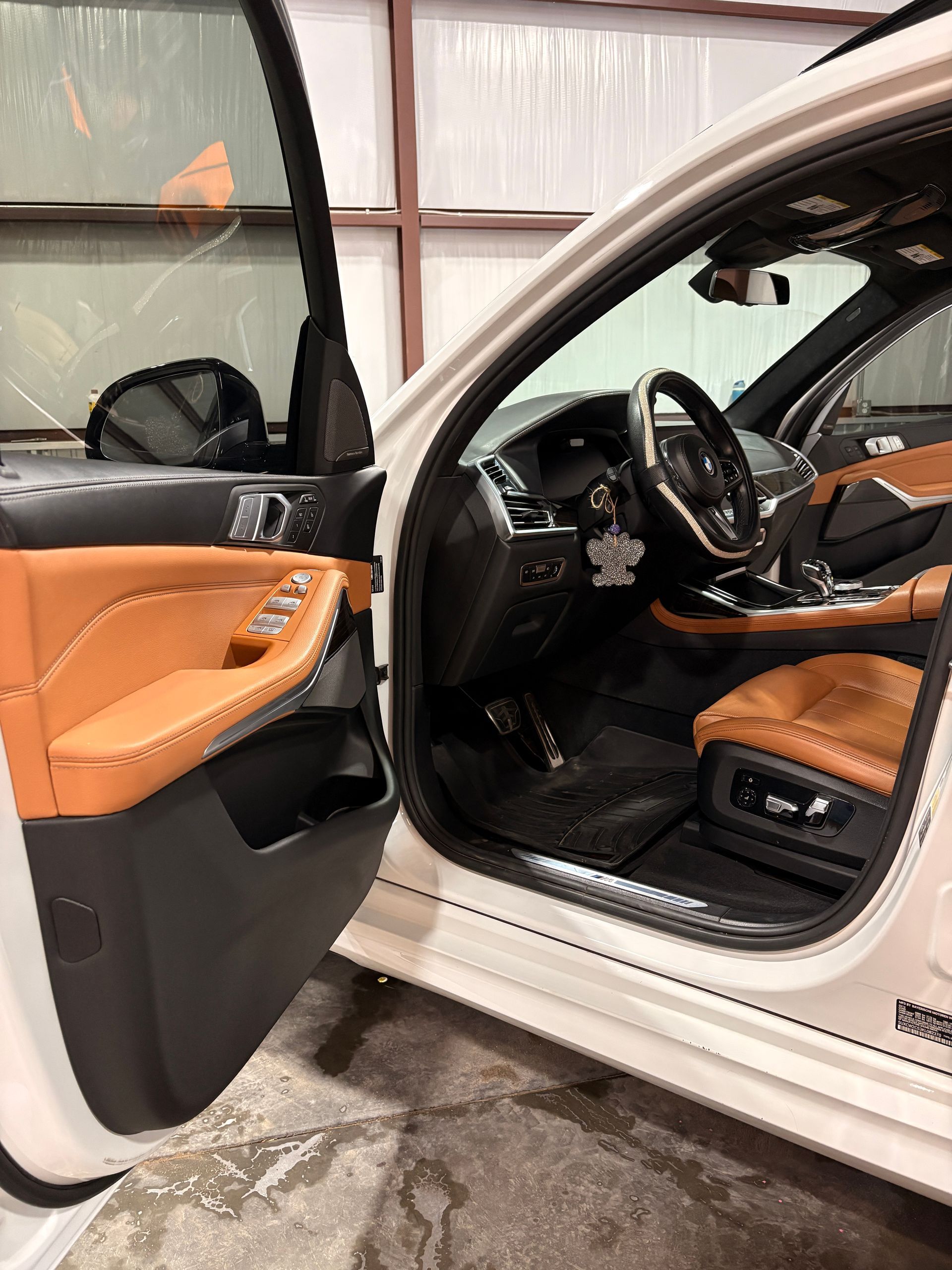 Open car door showing tan leather interior, steering wheel, and driver’s seat in a garage.
