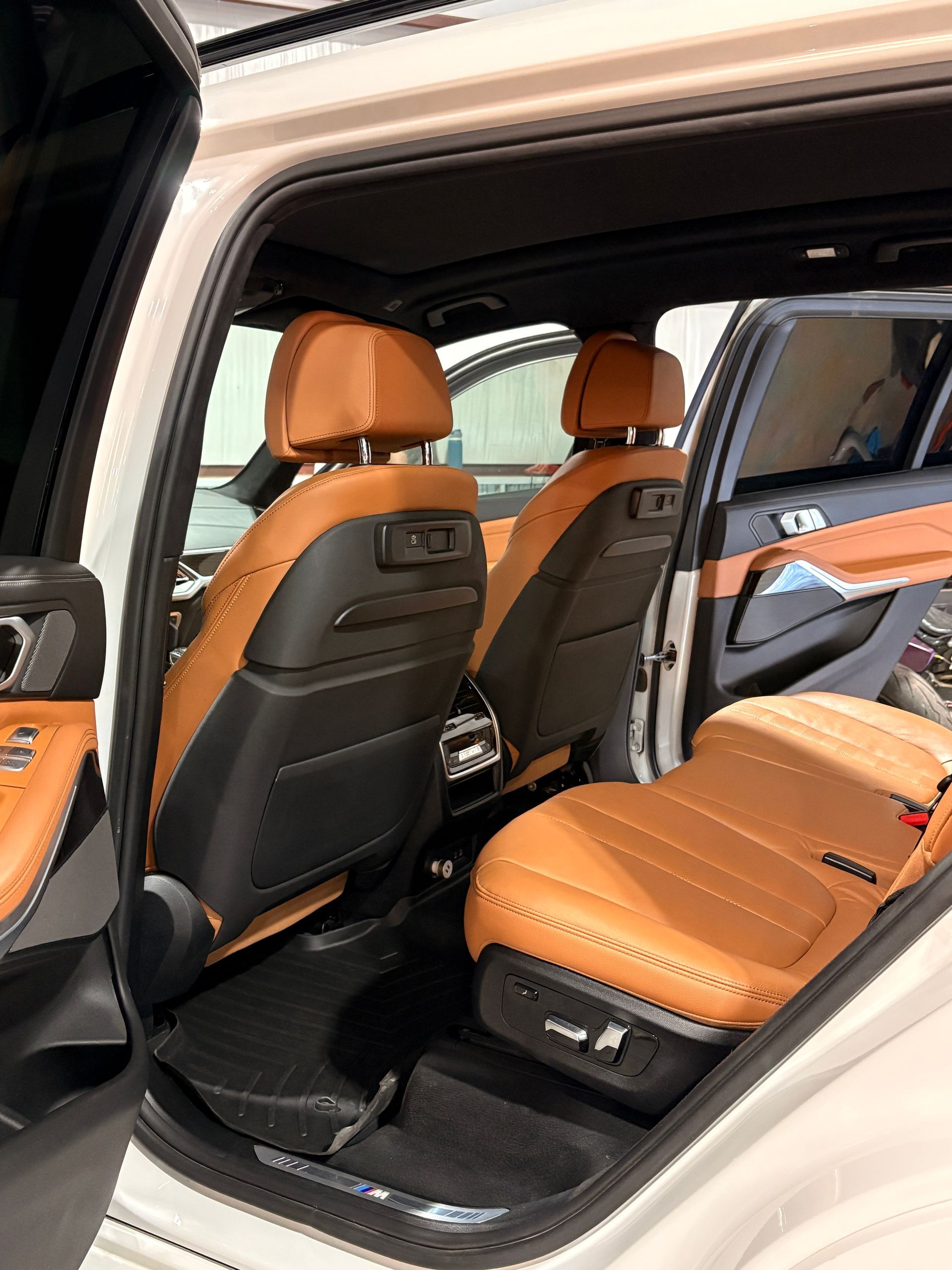 Car interior with tan leather seats and open rear door, showing back seat and front seat backs