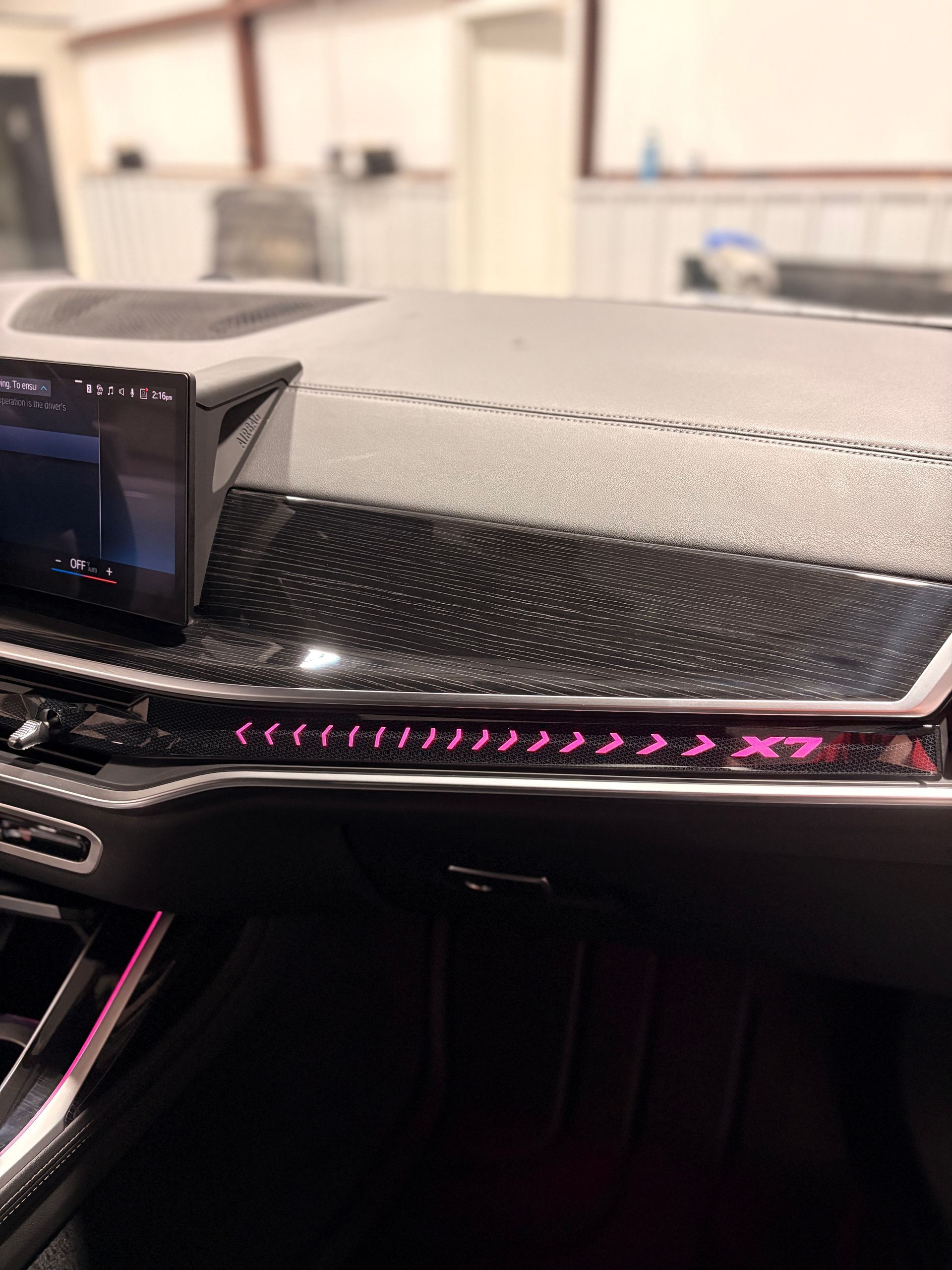 Car dashboard with a digital display and pink ambient lighting across the center console