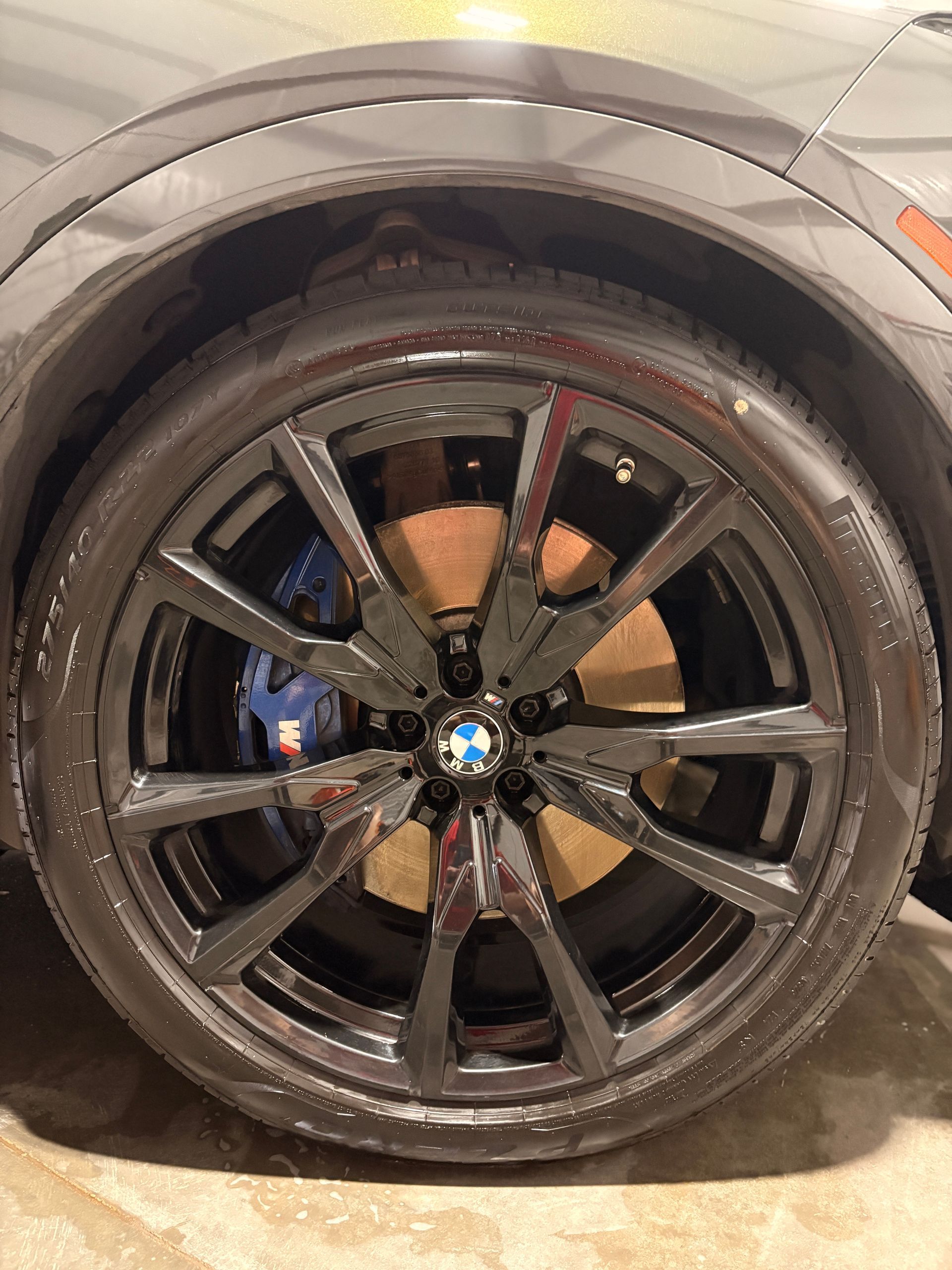 Close-up of a black BMW wheel and tire, wet with dirt, under a car’s wheel arch.