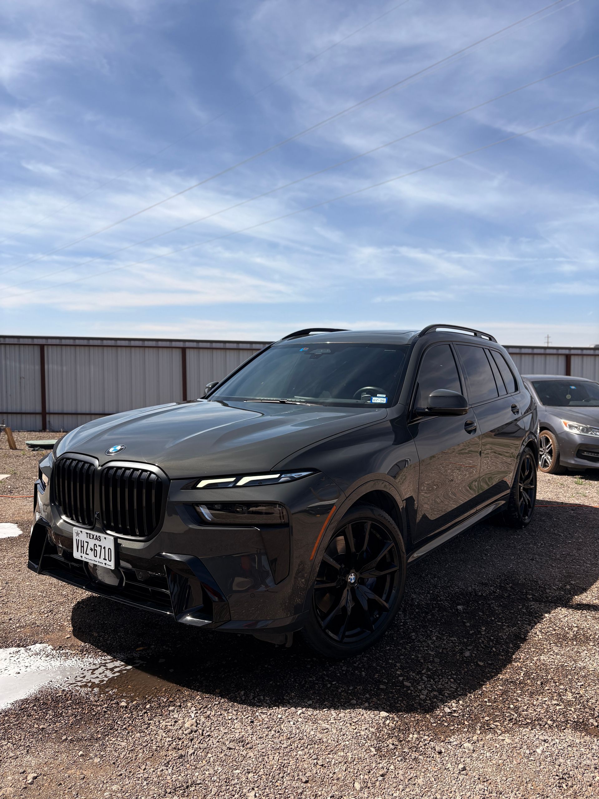 Black BMW SUV parked on gravel under a cloudy sky, front-left view