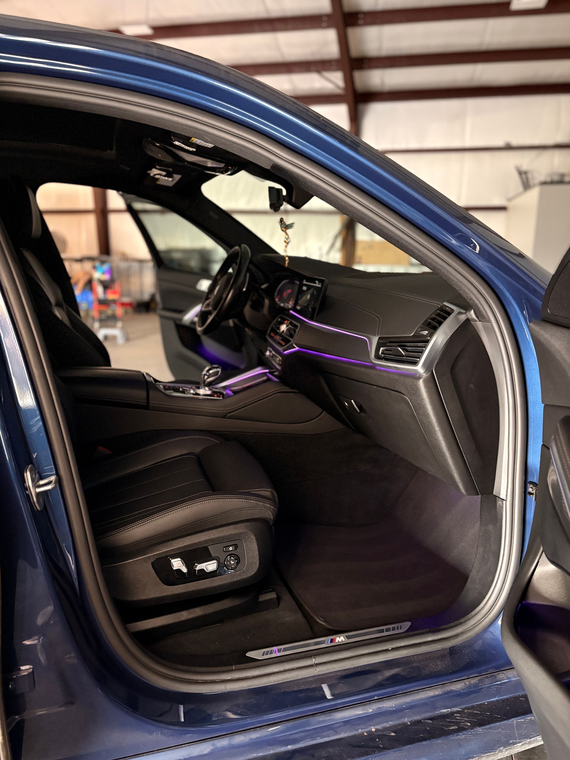 Blue car interior with purple ambient lighting and black leather seats, viewed through the open door