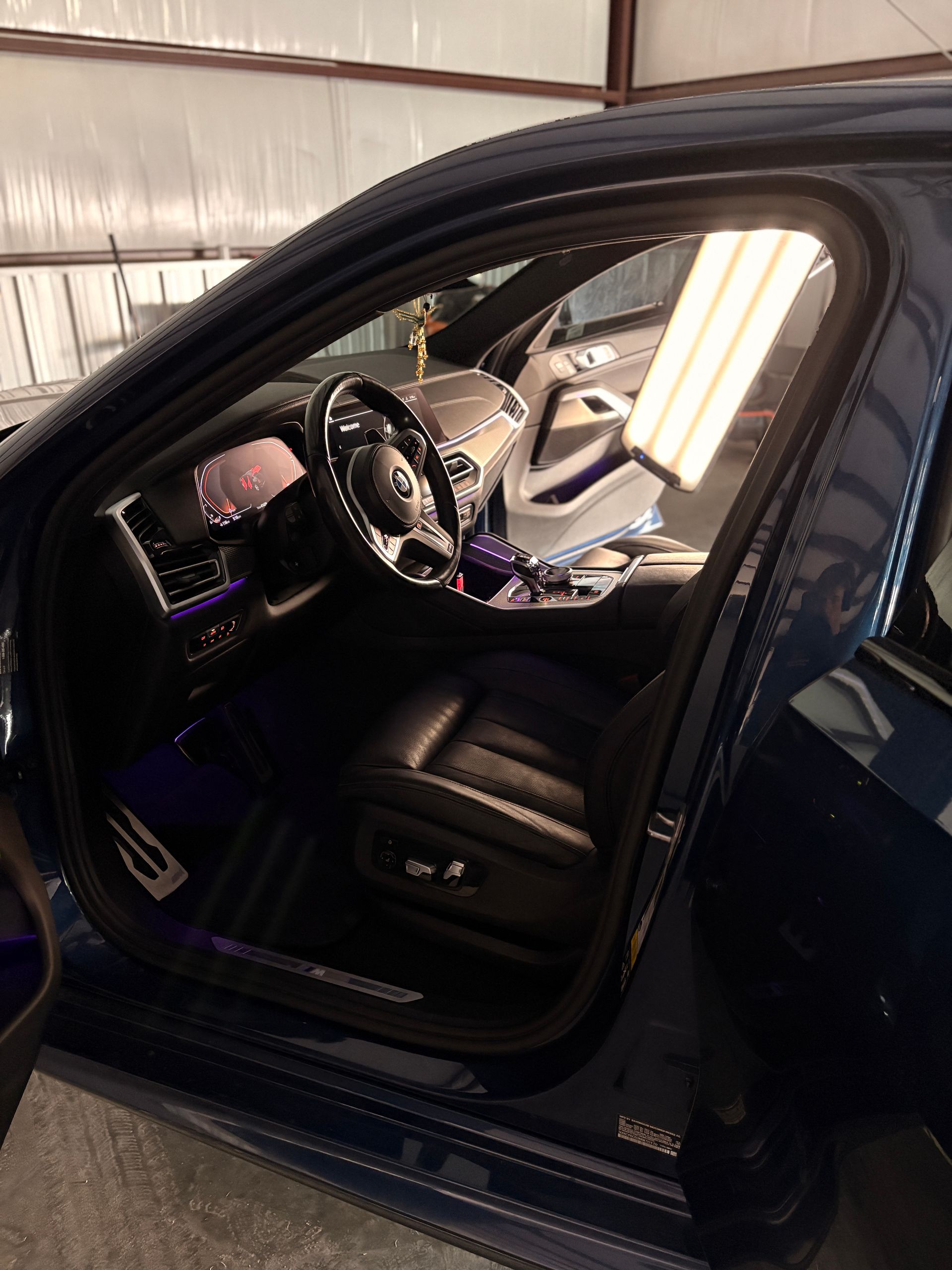 Open car door showing a black leather interior and steering wheel in a garage