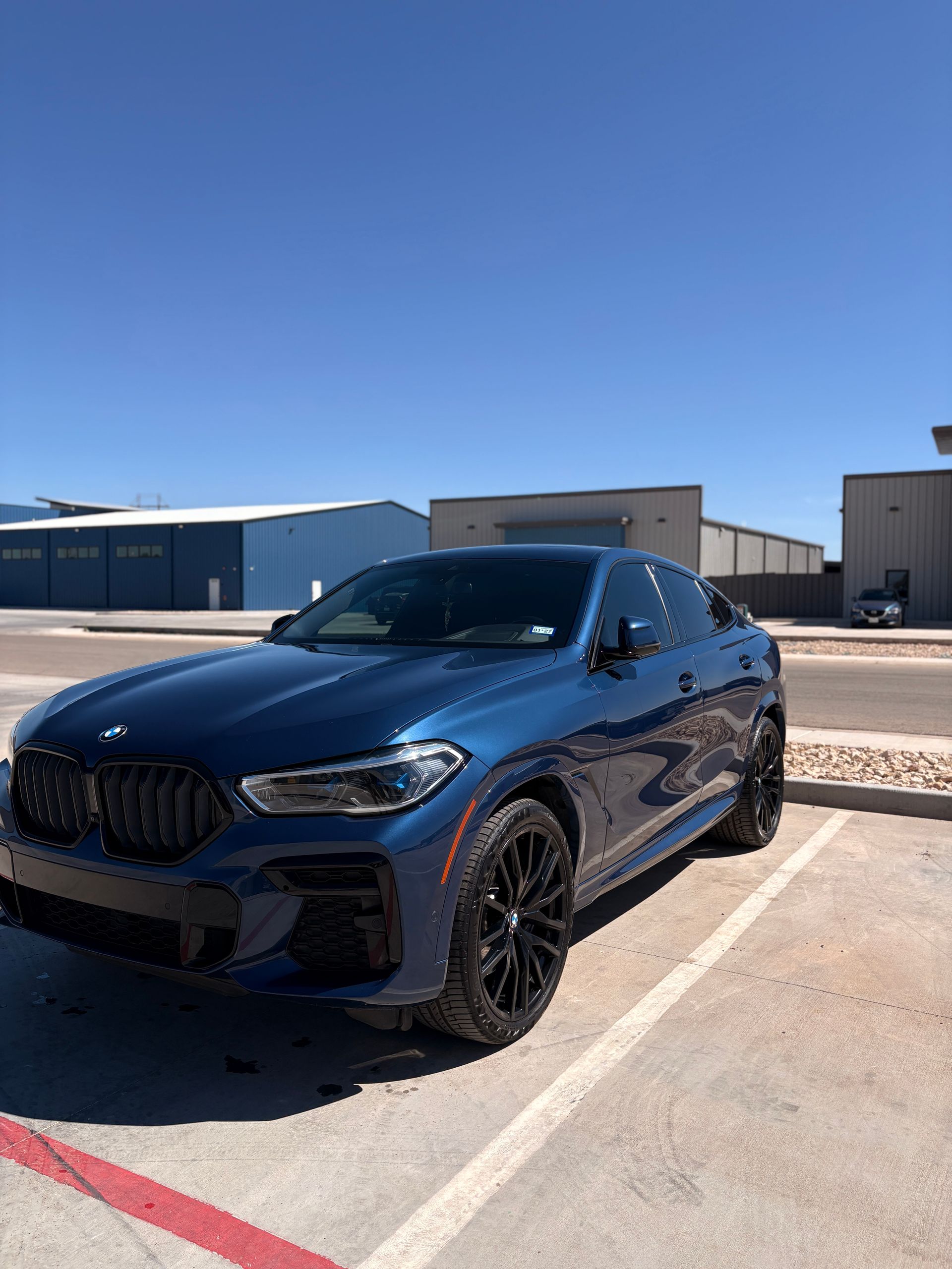Dark blue BMW SUV parked in a sunlit lot near industrial buildings.