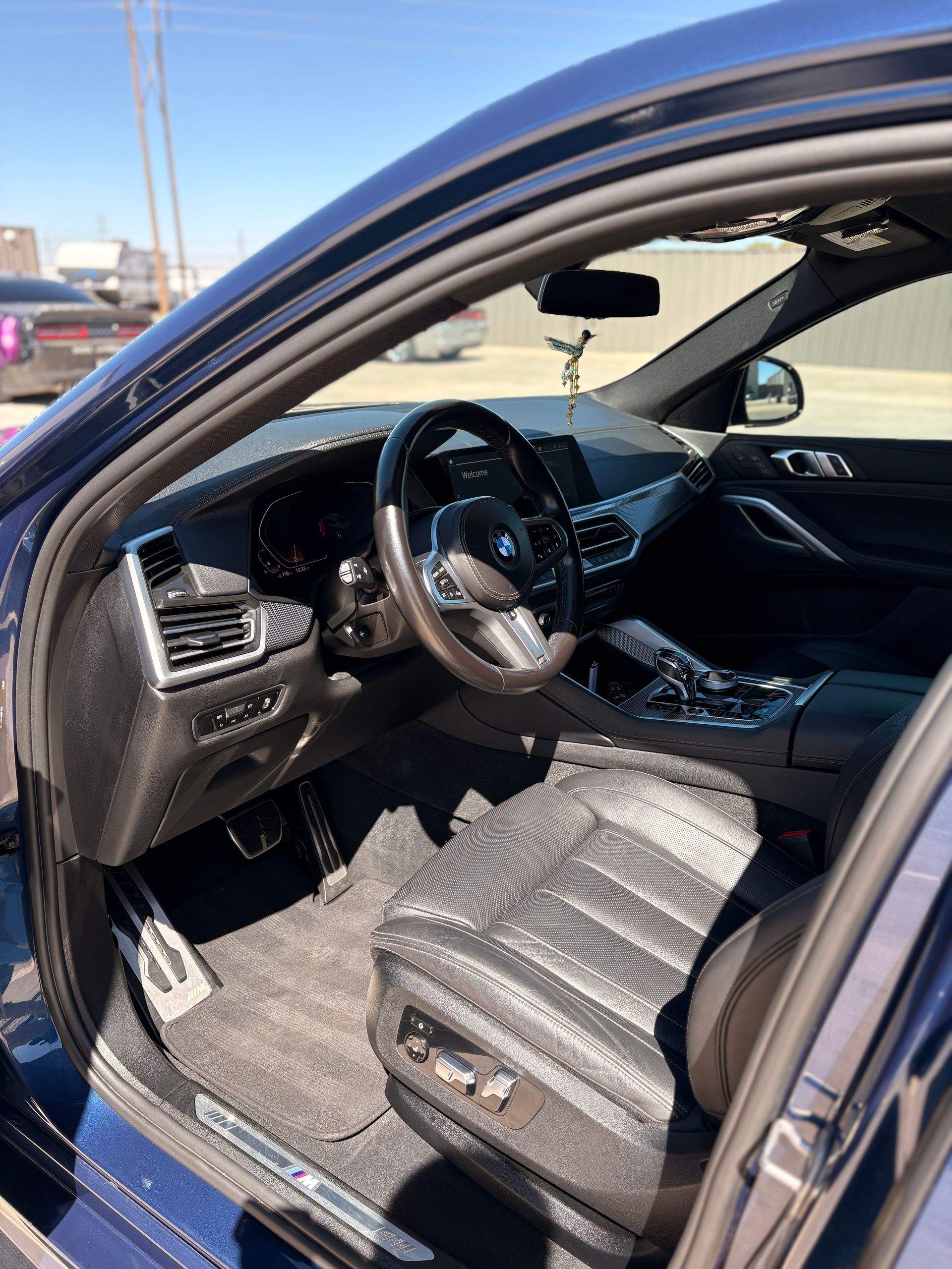 Open car with driver door ajar, showing black interior and steering wheel in a parking lot.