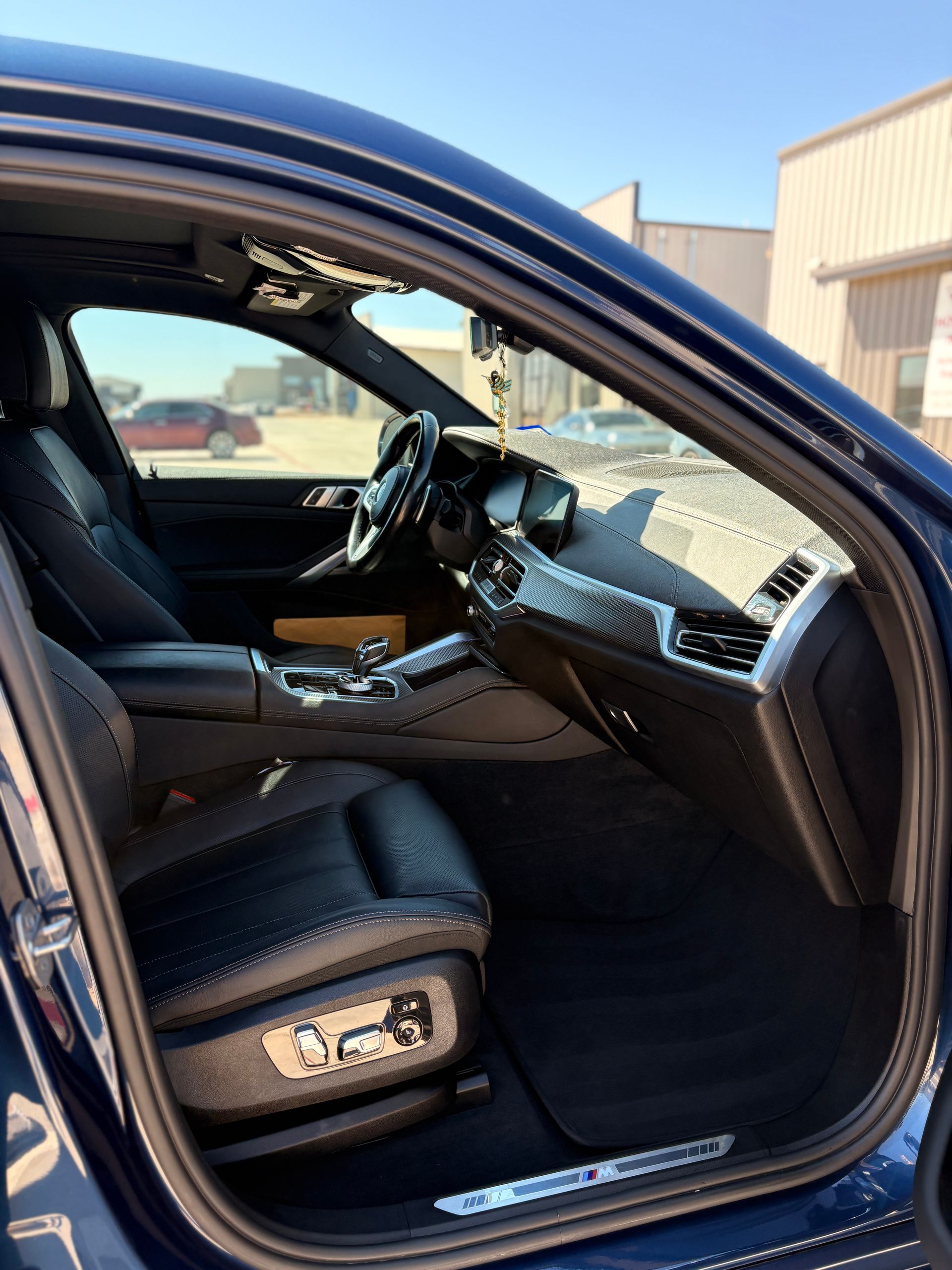 Luxury car interior with brown leather seats and dashboard, viewed through an open driver’s door