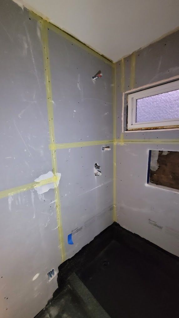 A bathroom under construction with a window and a gray wall.