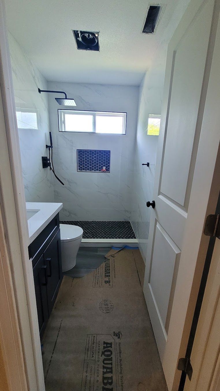 A bathroom with a toilet , sink , shower and window.