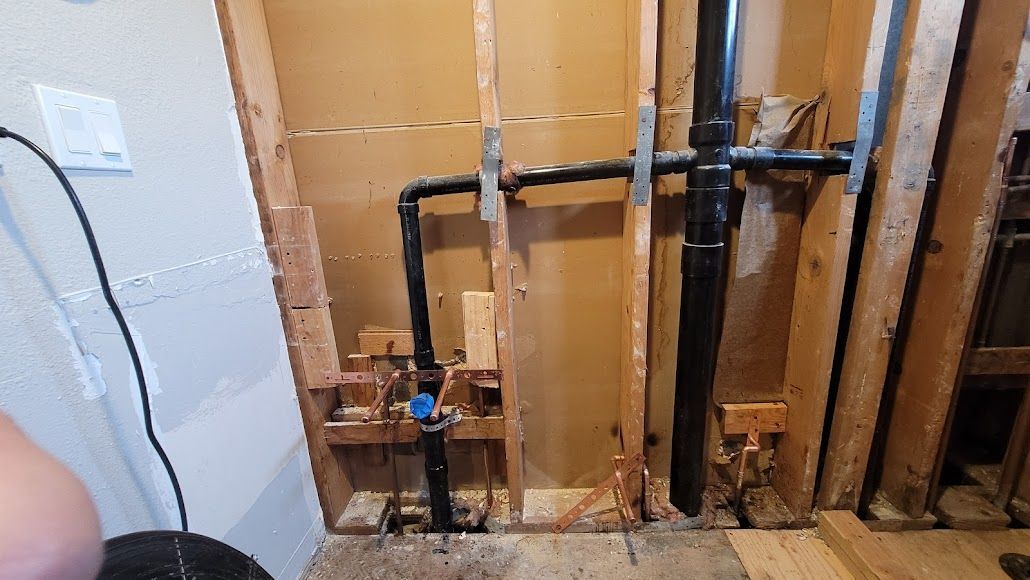 A person is holding a bucket in front of a wall with pipes coming out of it.