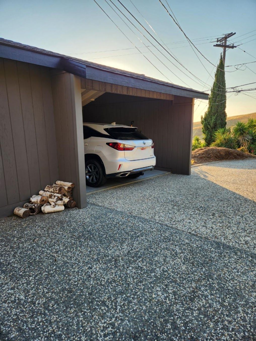 A white car is parked in a garage next to a pile of wood.