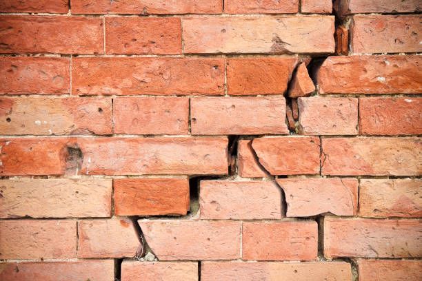 Cracked red brick wall; large vertical crack through several bricks, possible structural damage.