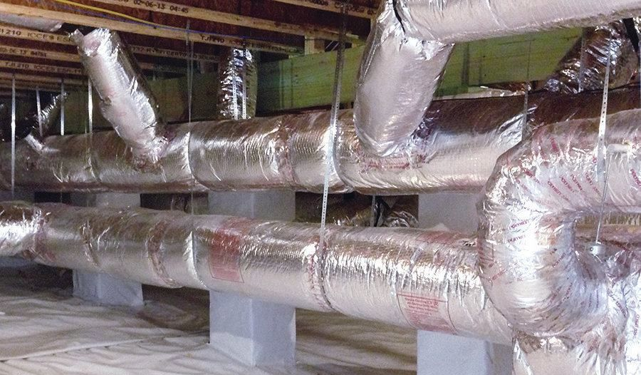 Insulated HVAC ductwork, silver, runs horizontally through a construction space, supported by concrete blocks.
