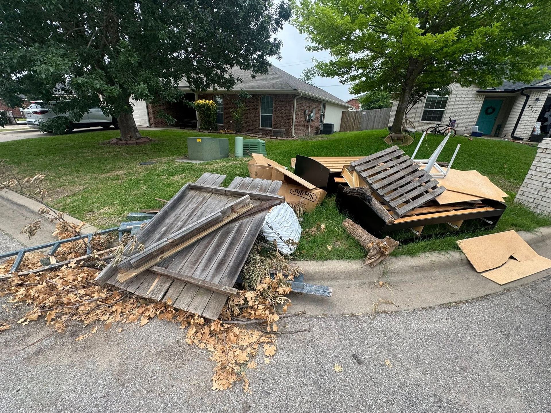 A pile of wooden pallets is sitting on the side of the road in front of a house.