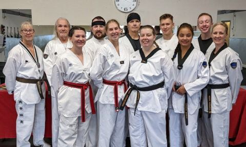Group of Taekwondo practitioners in white uniforms, posing indoors.