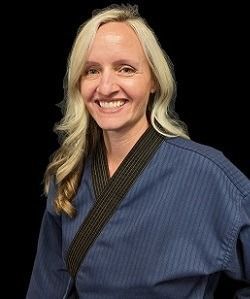 Woman in a blue martial arts uniform smiles, black belt visible. Black background.