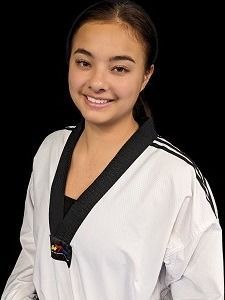 Woman in white taekwondo uniform smiling, black background.