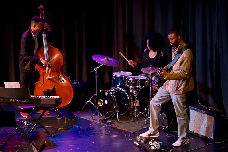 Jazz band on stage: bassist, drummer, guitarist, and keyboard.