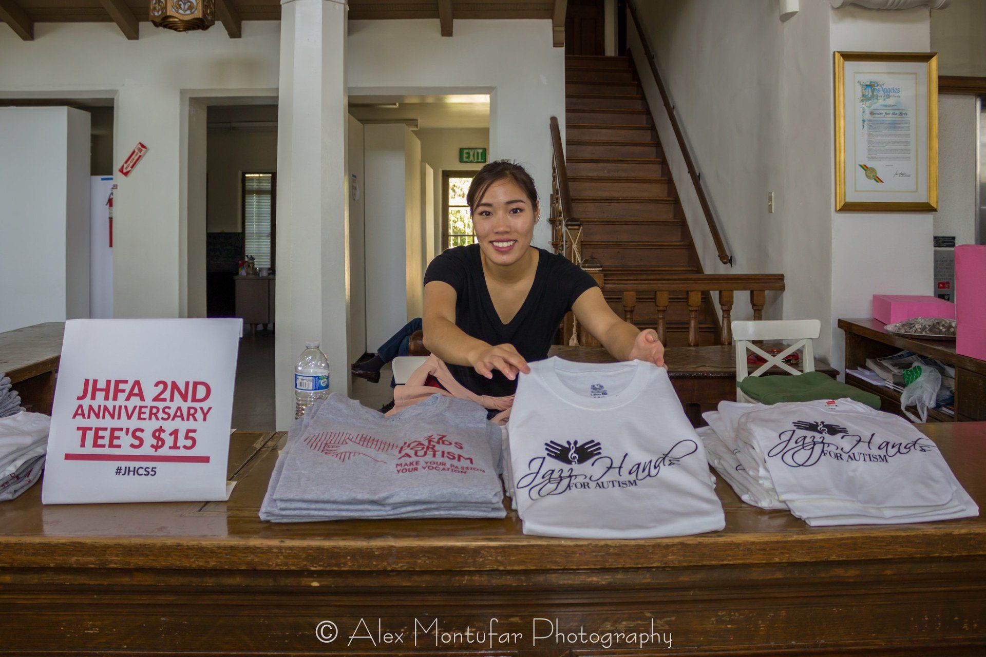 Woman at a table with shirts for sale; 