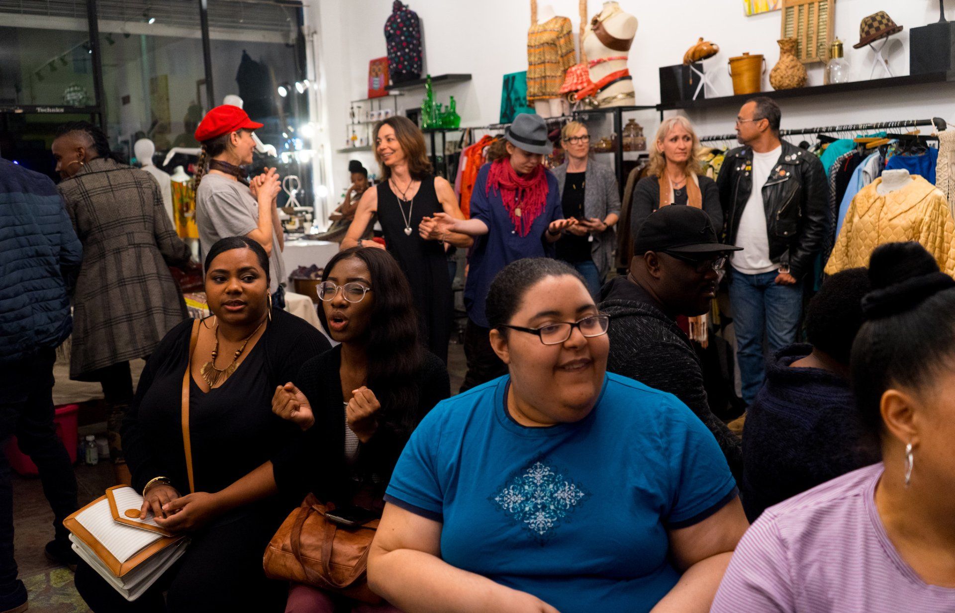 People at an event inside a store. Several people are smiling, others look around. Clothing and items on display.