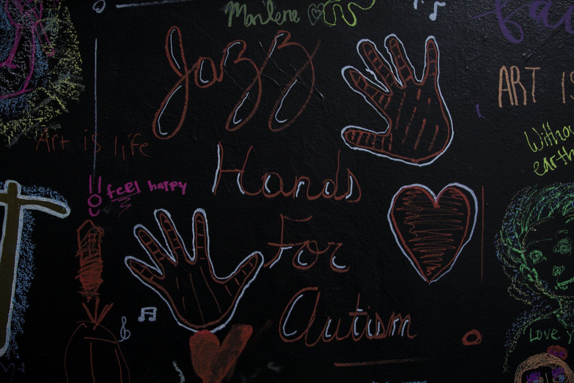 Black chalkboard with colorful chalk drawings, including hands, a heart, and the words 