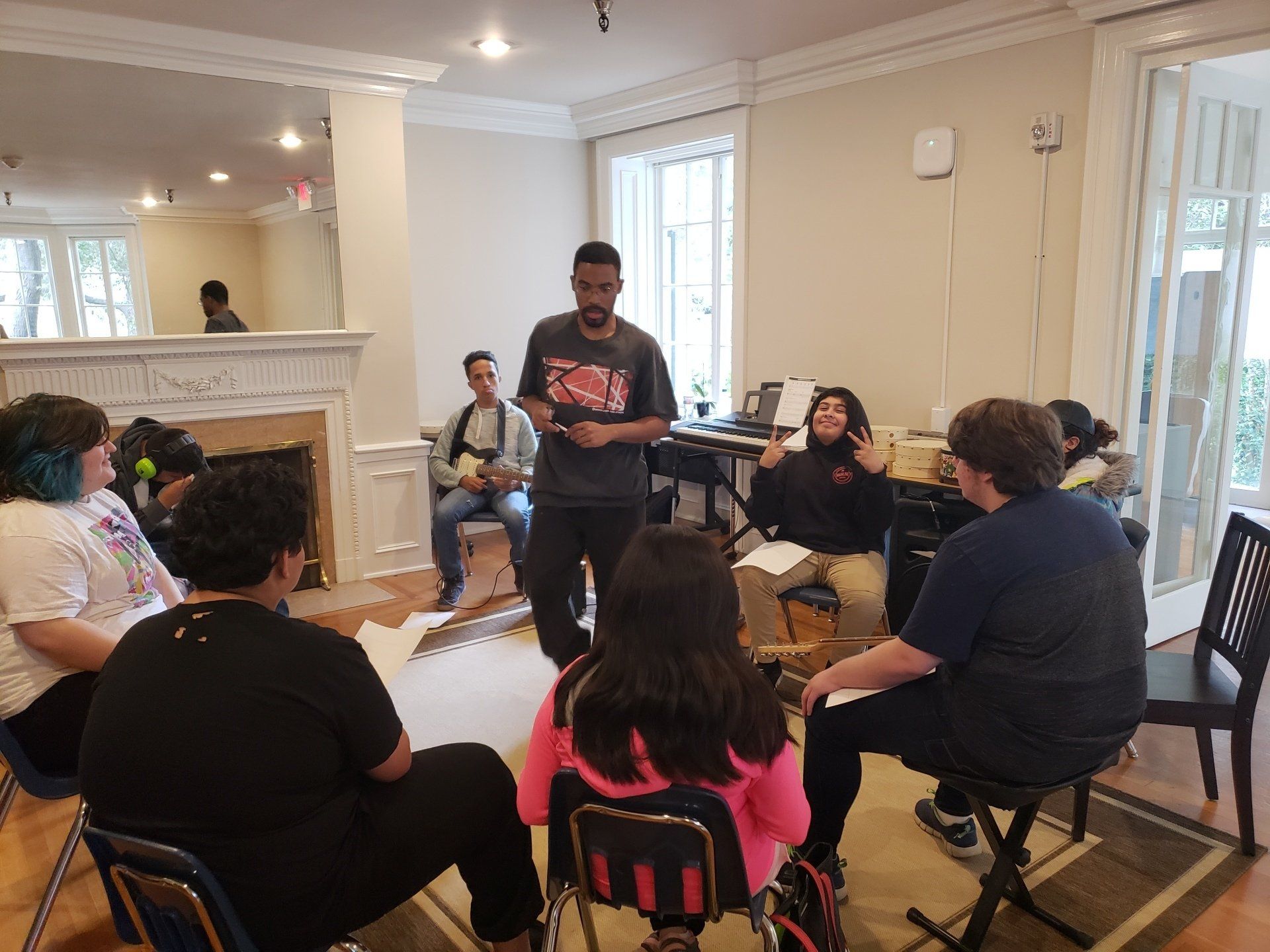 A group of young people in a room listening to a man who is standing, talking.