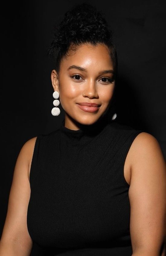 Woman with dark hair pulled up, wearing a black top and white drop earrings, smiling at the camera.