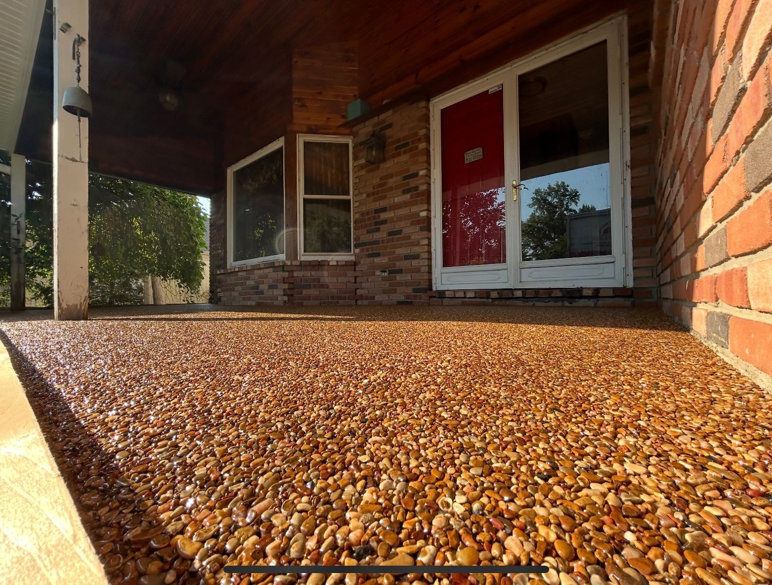 A sunny patio with a resin-bound gravel floor, brick house exterior, and glass doors with a red panel.