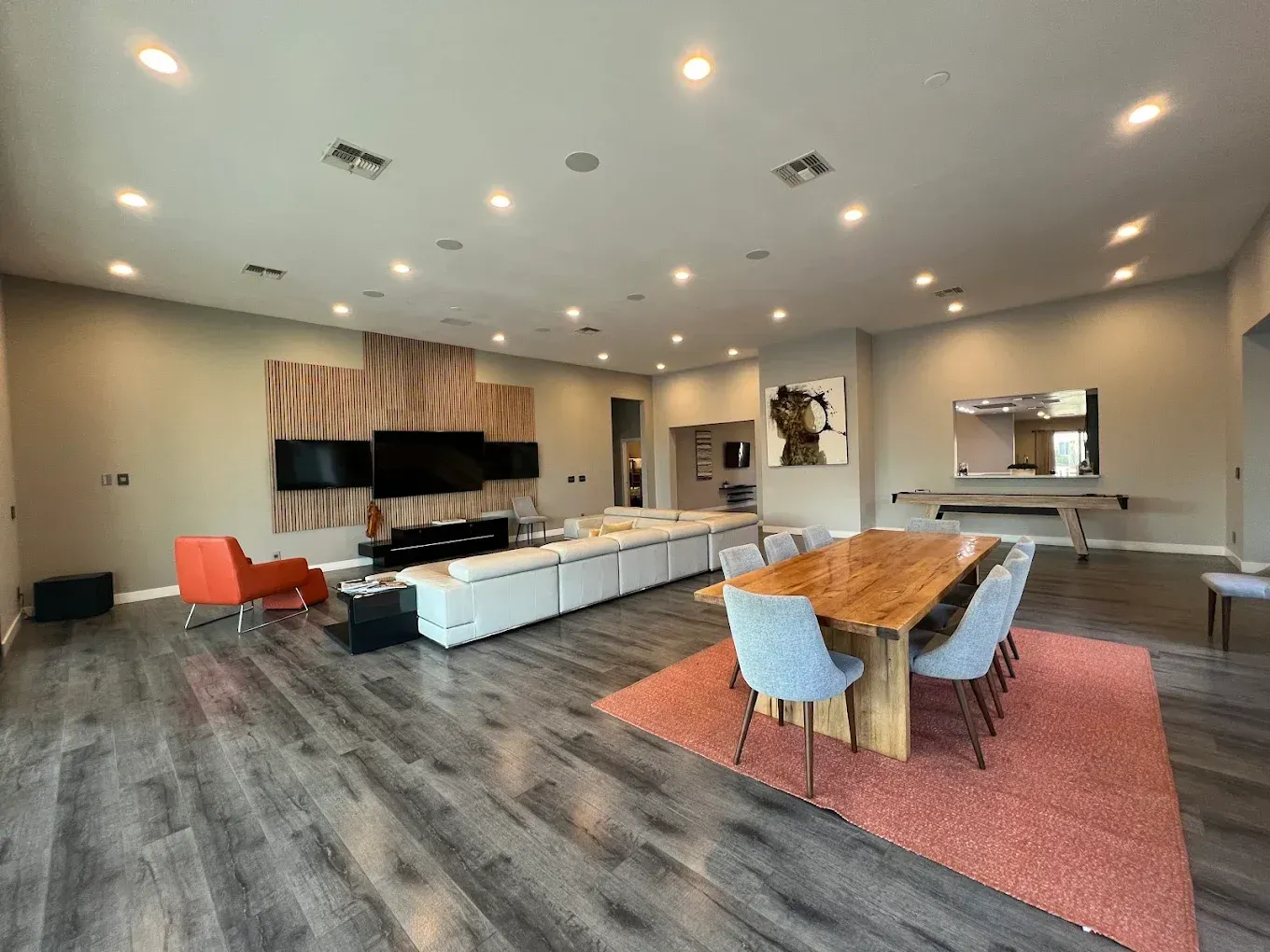 Spacious modern living room with wood floors, recessed lighting, long sofa, dining table, and ping pong table.