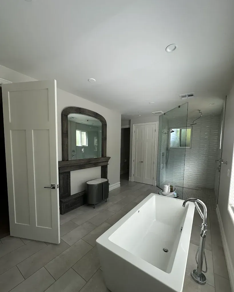 Modern bathroom with a white bathtub, glass shower, large mirror, and light gray tile flooring.