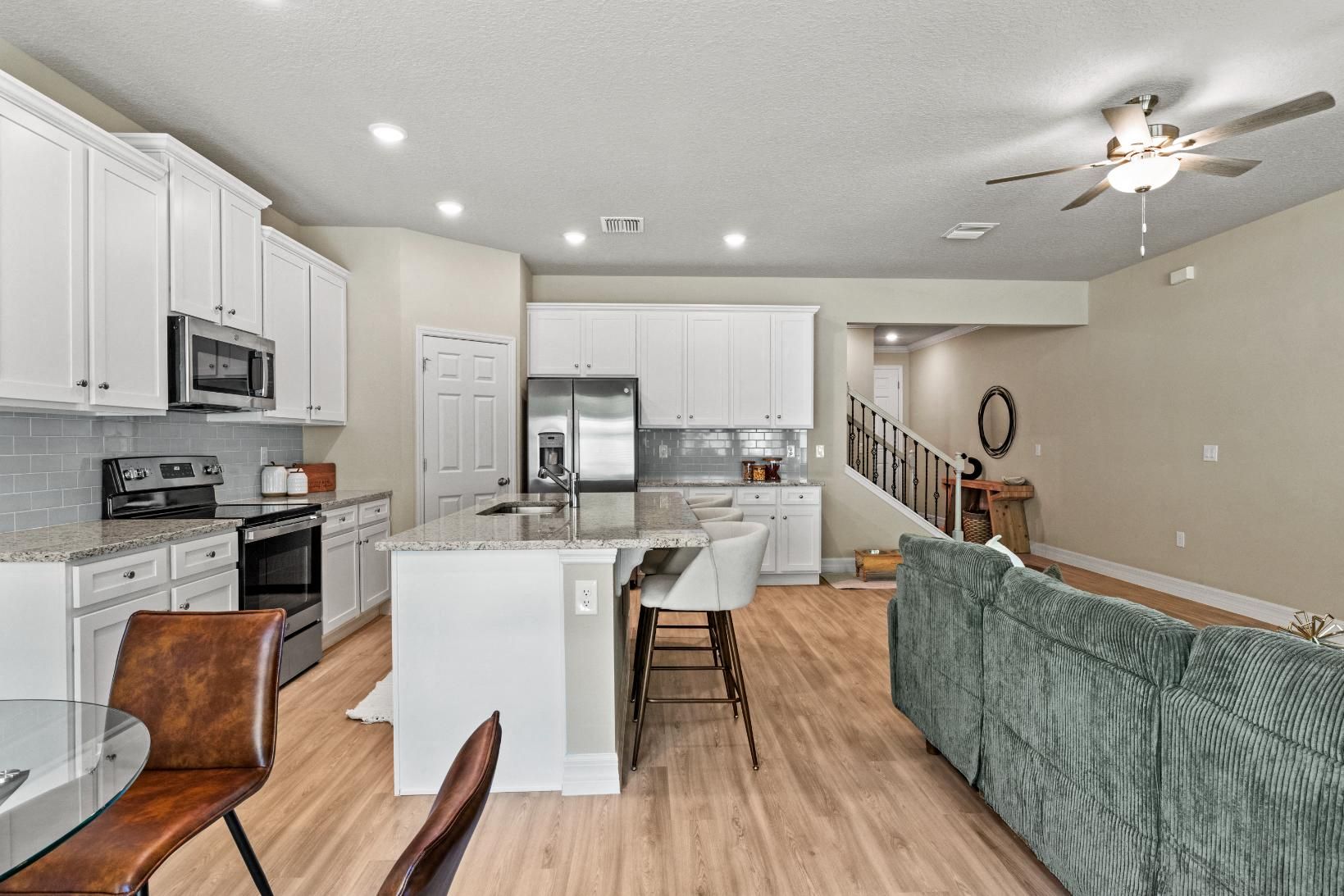 A kitchen with white cabinets , a stove , a refrigerator , a microwave and a ceiling fan.