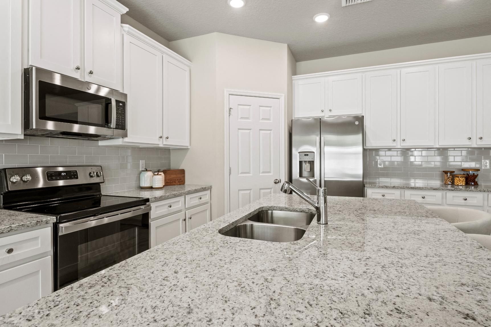 A kitchen with granite counter tops , stainless steel appliances , and white cabinets.