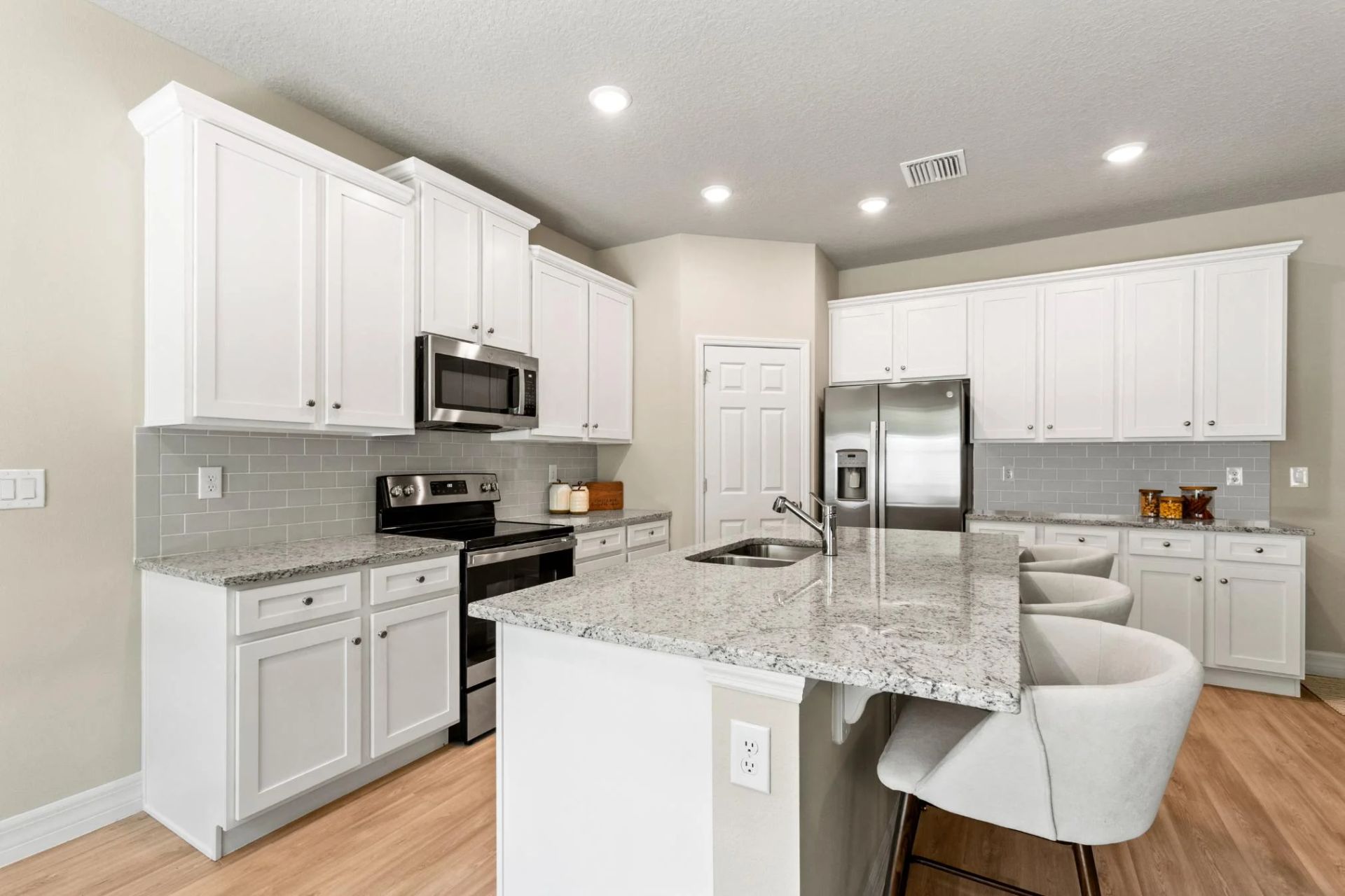 A kitchen with white cabinets , granite counter tops , stainless steel appliances and a large island.