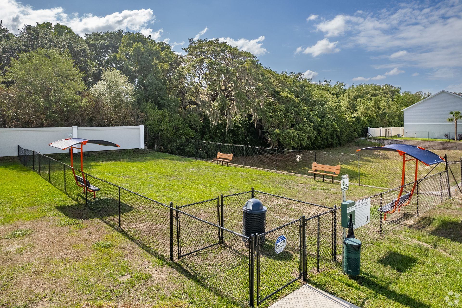 A dog park with a fence surrounding it and trees in the background.