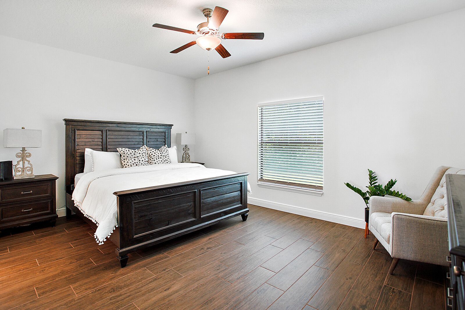 A bedroom with a king size bed , a chair , a ceiling fan , and two windows.