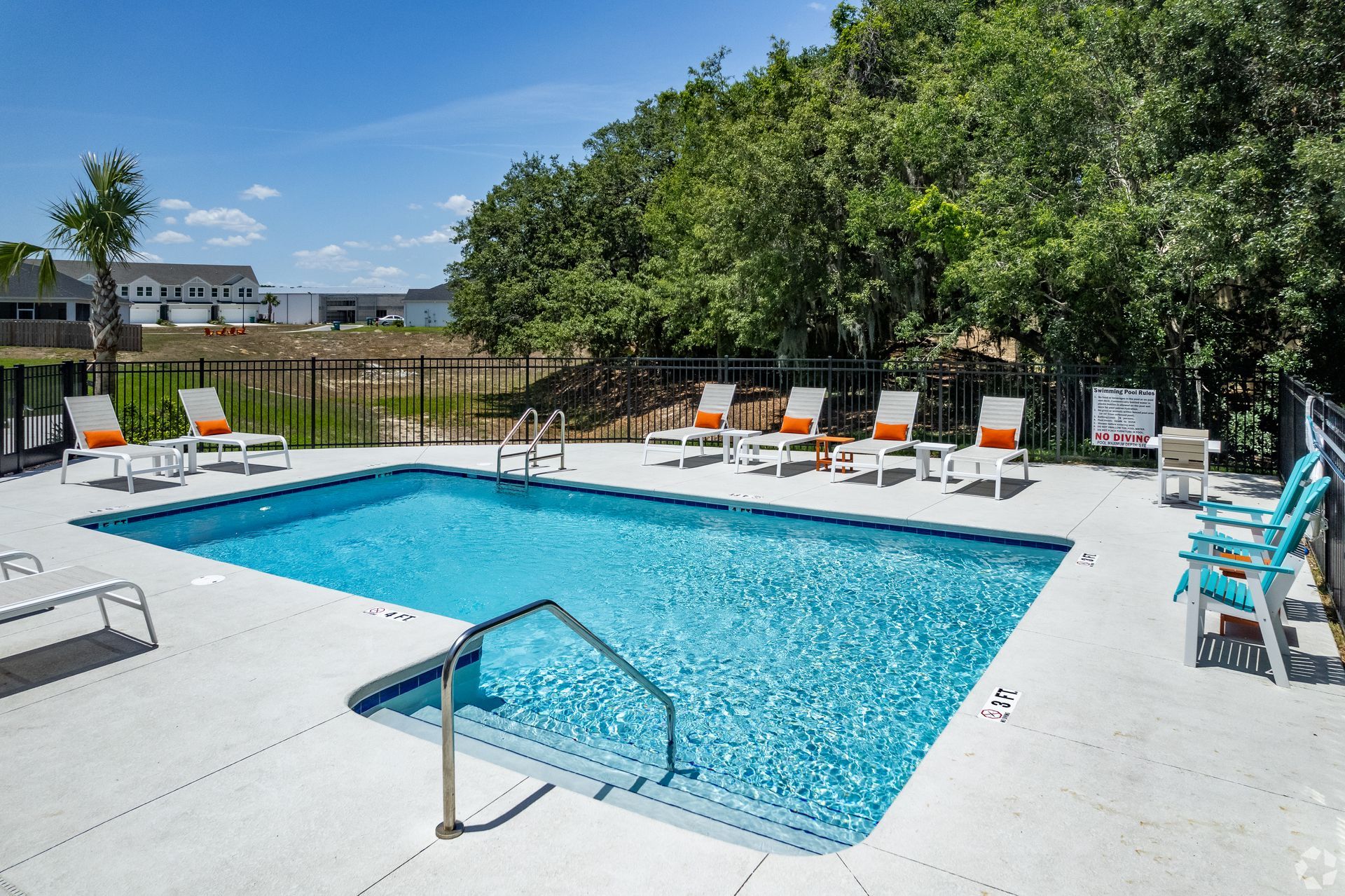 A large swimming pool surrounded by chairs and trees on a sunny day.