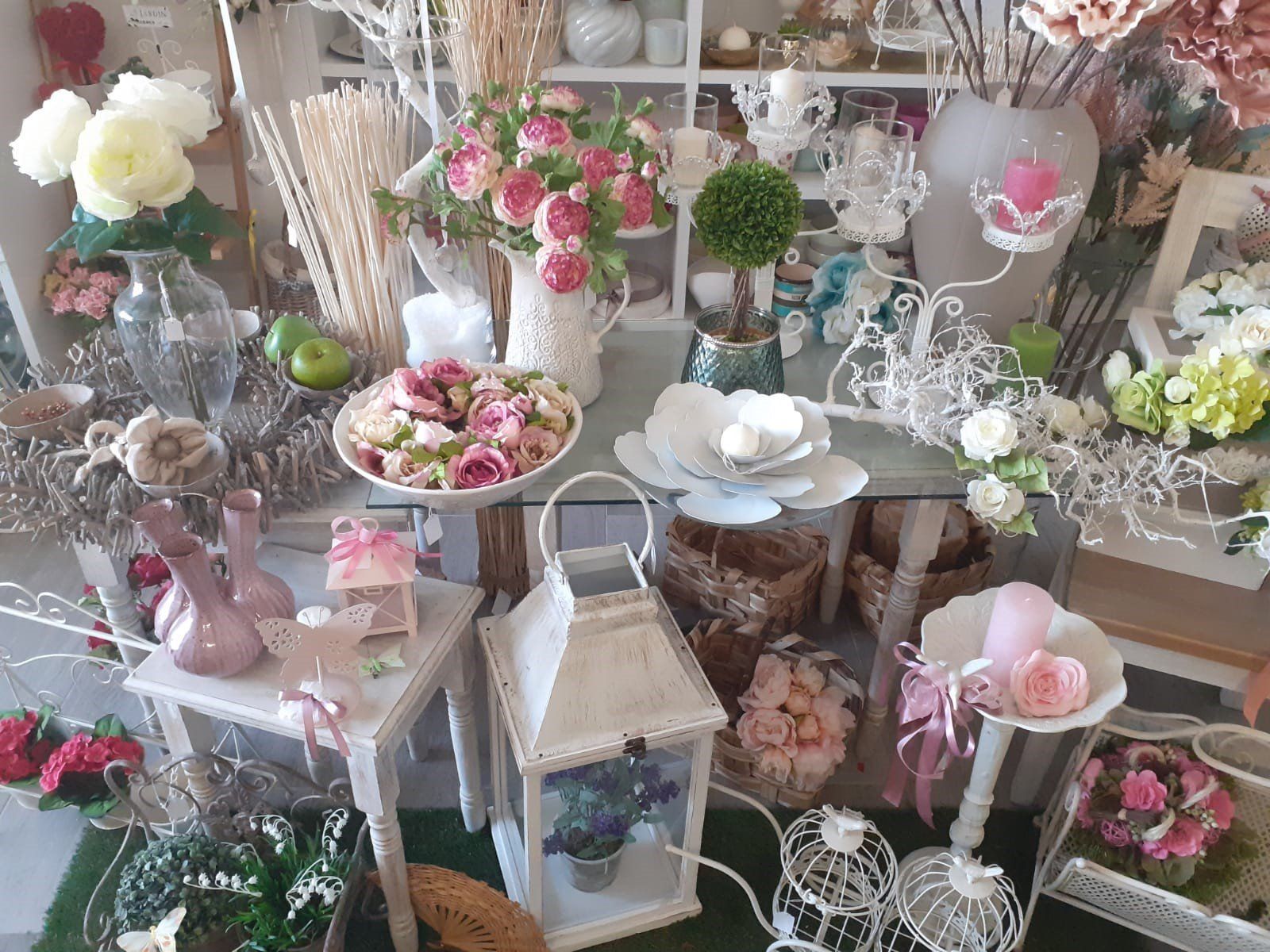 Esposizione di fiori e composizioni decorative, per lo più rosa e bianchi, su scaffali e tavoli.