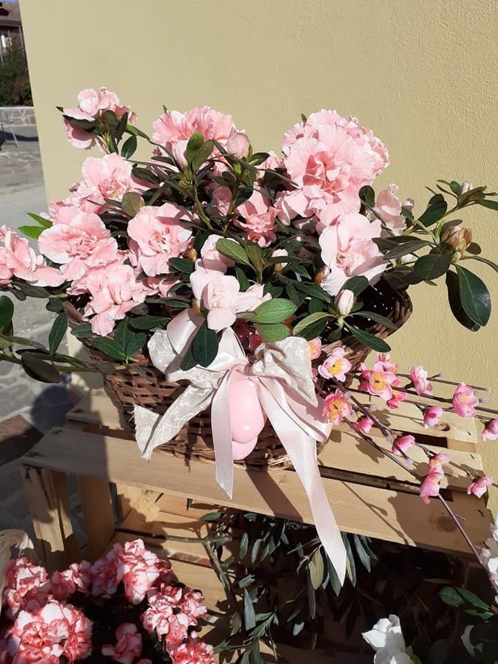 Fiori di azalea rosa in un cestino intrecciato con un uovo di Pasqua decorato con un nastro, posto su una cassa di legno.