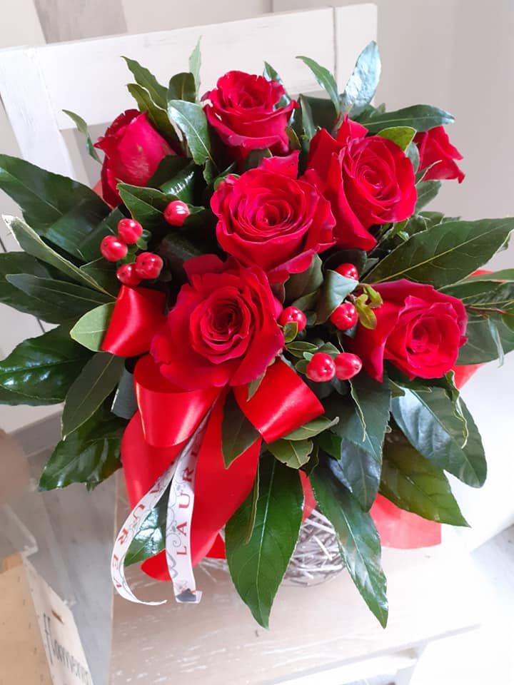 Rose rosse in una composizione floreale rotonda con nastro rosso e verde.