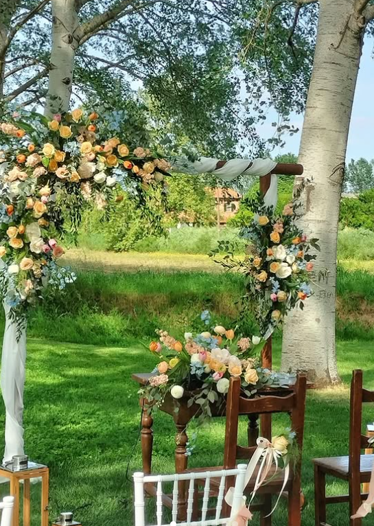 Arco nuziale decorato con fiori in un ambiente da giardino; tavolo e sedie sistemati nelle vicinanze.