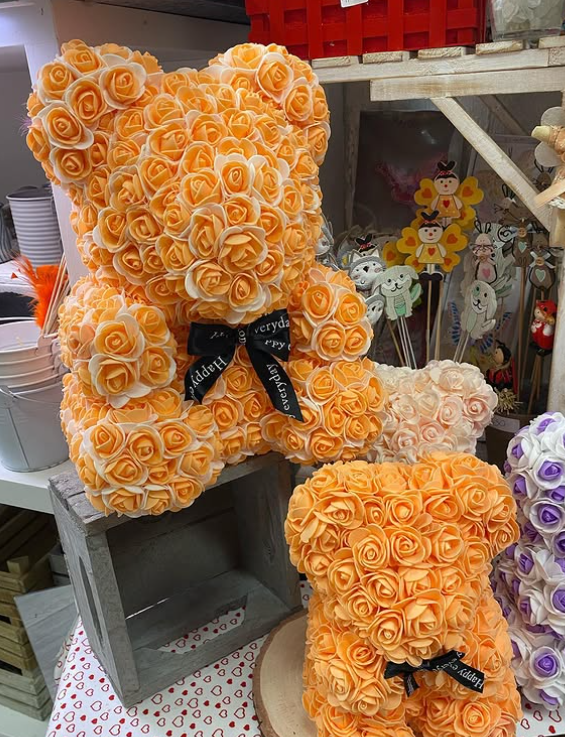 Statuette di orsacchiotti ricoperte di rose arancioni con fiocchi neri. Un orsetto più piccolo è esposto in negozio.