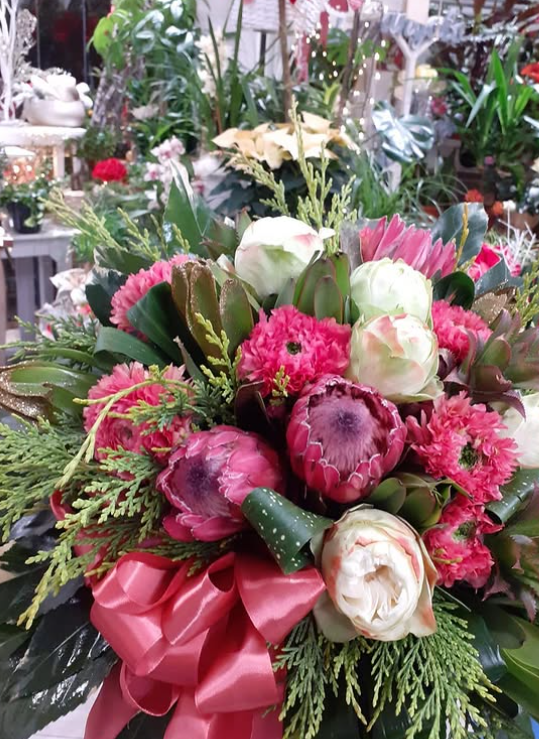 Primo piano di una composizione floreale colorata con fiori rosa e bianchi, verde e un fiocco rosso.