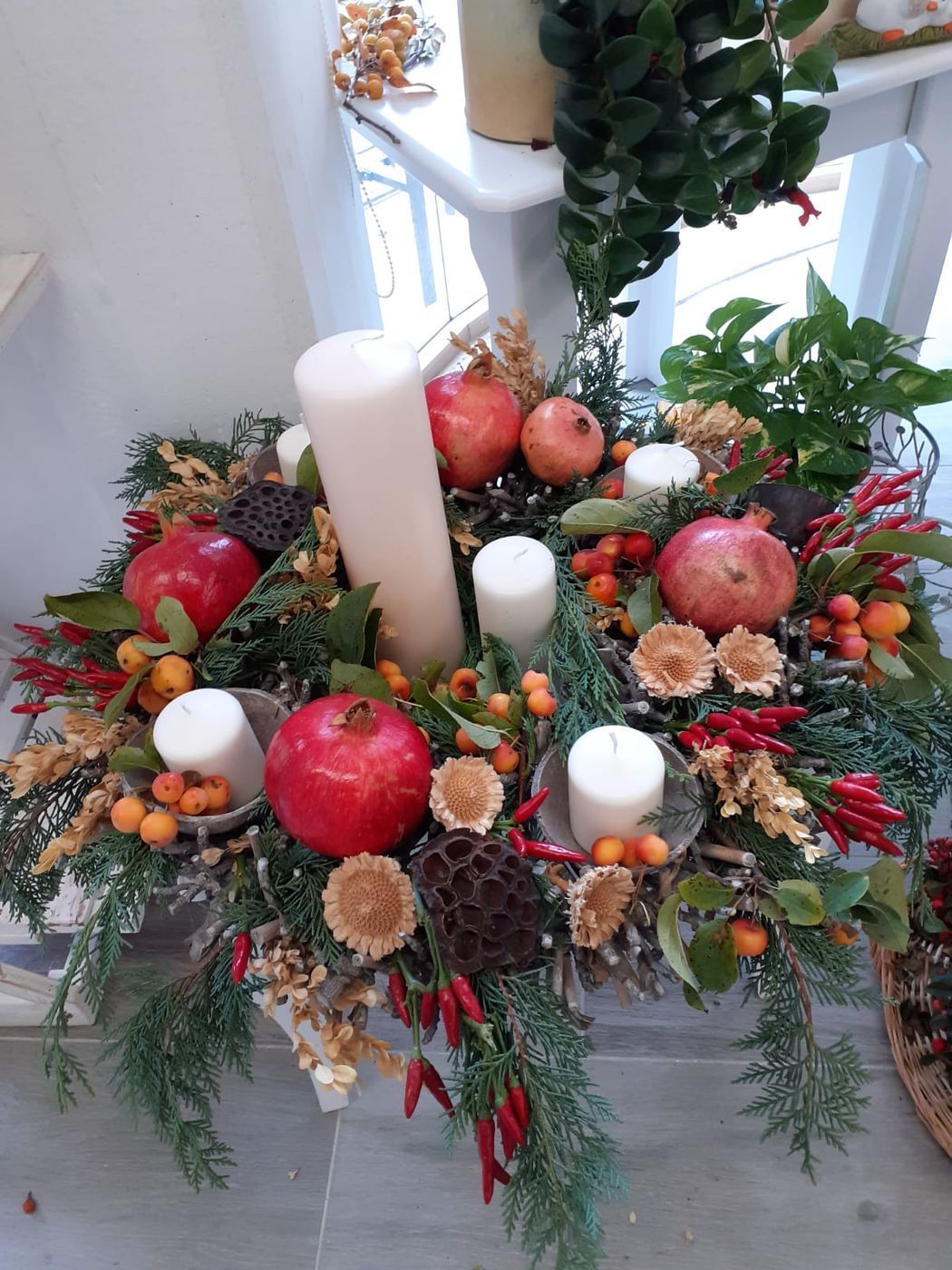 Composizione floreale con melograni, candele e verde.