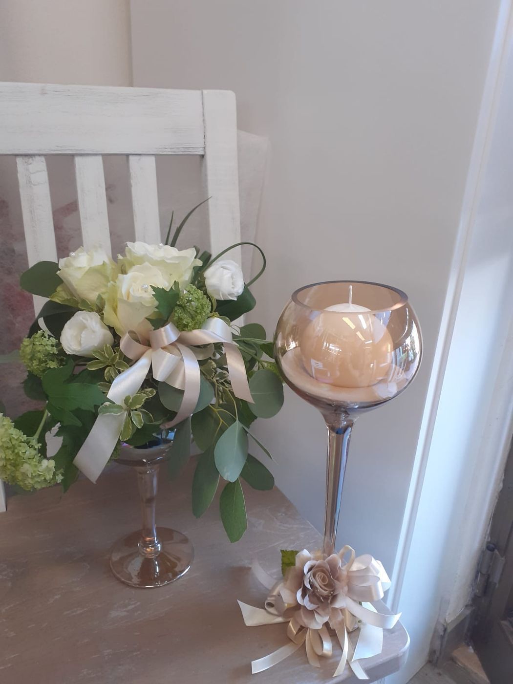Composizione floreale con rose bianche e candela in un portacandele di vetro.