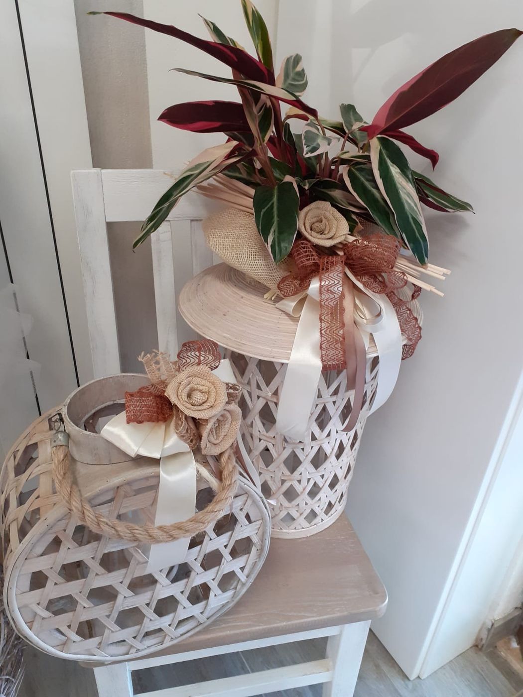 Due cestini decorativi in ​​vimini, uno con piante e nastro, su una sedia bianca.