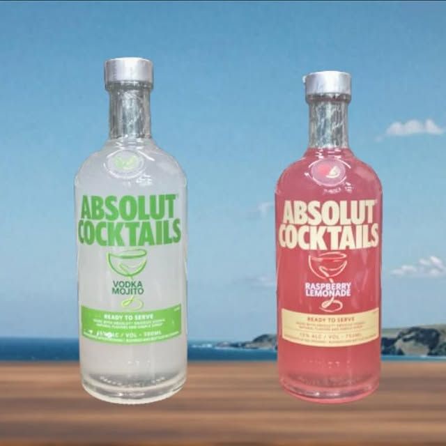 Two bottles of absolut cocktails sit on a wooden table