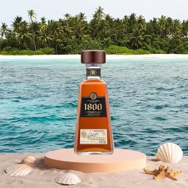 A bottle of 1800 tequila is sitting on a beach